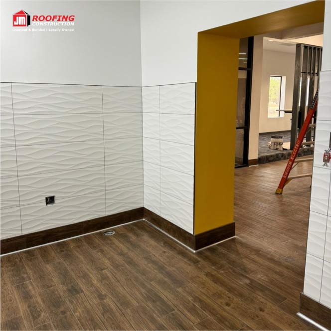 Interior remodeling project by JM Roofing Construction in El Paso. The image shows a professionally finished commercial or residential floor, featuring textured white wall tiles, a dark wood-style tile baseboard, and brown wood-look floor tiles. This high-quality flooring and tile installation is often completed as part of a full home painting and remodeling service, reflecting our commitment to quality craftsmanship