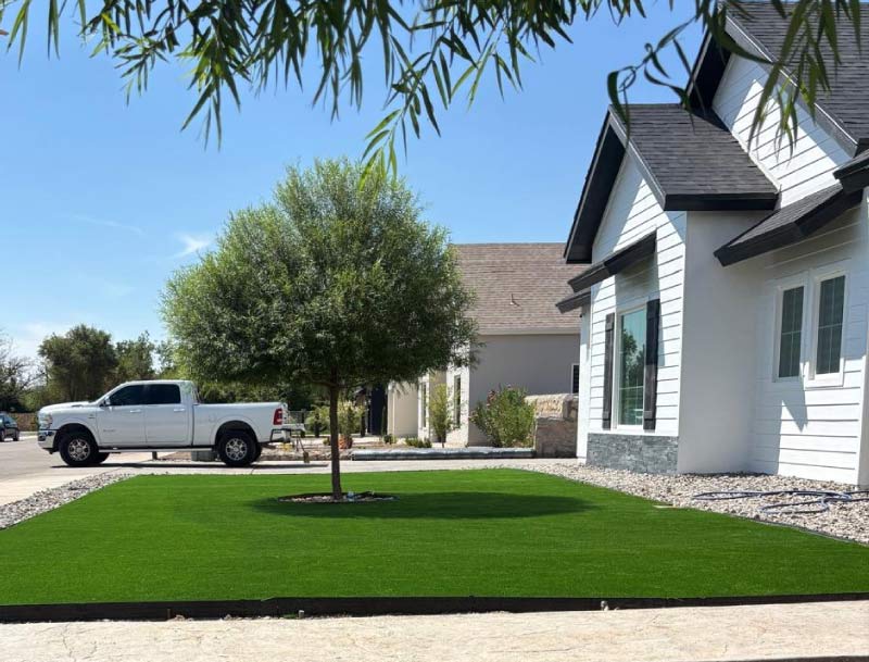 Front exterior view of a modern white house in El Paso featuring high-quality landscaping by JM Roofing Construction. The yard is neatly finished with maintenance-free artificial turf bordered by a dark frame, surrounded by white river rock, demonstrating our exterior services. This curb appeal is often achieved in conjunction with exterior and interior house painting projects to maximize property value