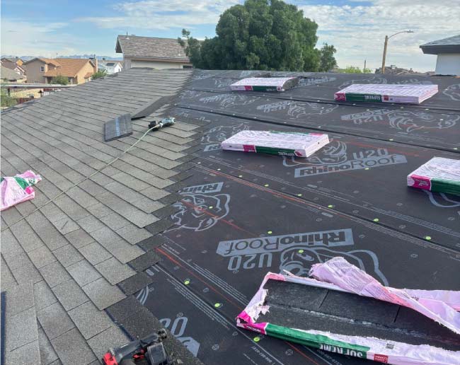 Close-up of JM Roofing crew installing new gray asphalt shingles over RhinoRoof underlayment during a partial tear-off and roof replacement project.