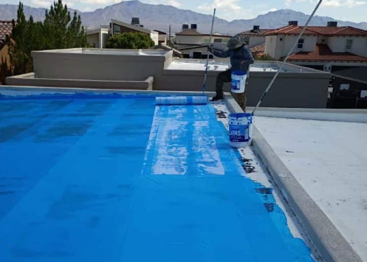 JM Roofing team member applying a blue primer layer to a flat roof, demonstrating the detailed multi-step process for a long-lasting GAF Coating Pro system.