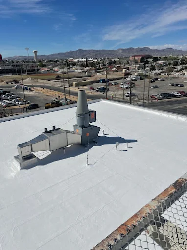 A wide-angle view of a completed white TPO flat roof installation in El Paso, featuring a clean, reflective membrane surface and industrial ventilation equipment against a mountain backdrop.