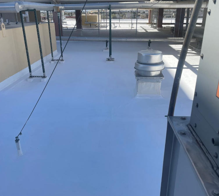 A high-angle view of a newly applied white silicone roof coating on a commercial flat roof, showing a seamless, reflective surface around HVAC units and vents.