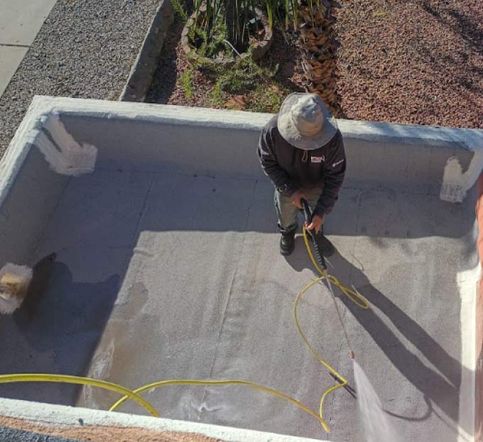 Professional JM Roofing technician using a high-pressure power washer to clean a flat roof surface in preparation for a high-quality coating application.