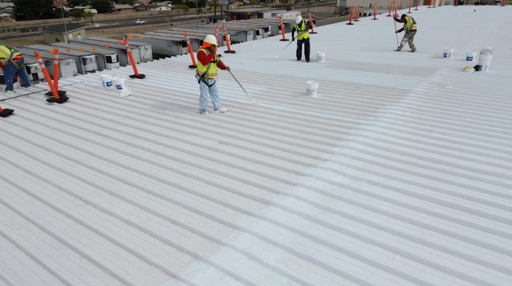 Professional application of a white reflective roof coating on a flat residential roof in El Paso.