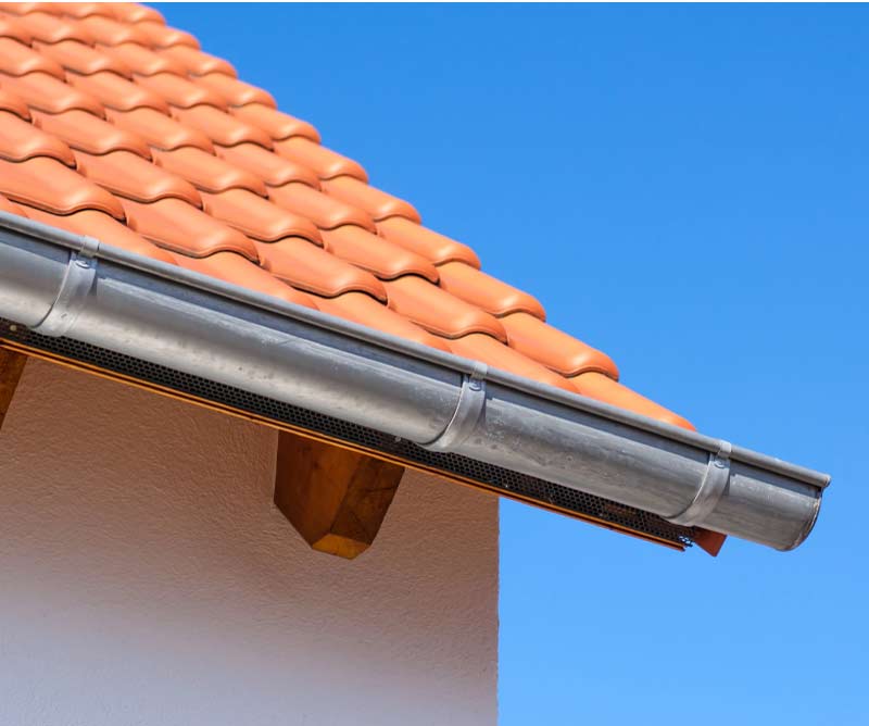 Angle view of bright orange terracotta roof tiles paired with a durable aluminum gutter and gutter guard system after gutter installation in el paso, tx