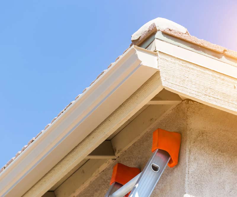 Professional gutter installation on a residential roof eave using a safety ladder with orange wall bumpers.