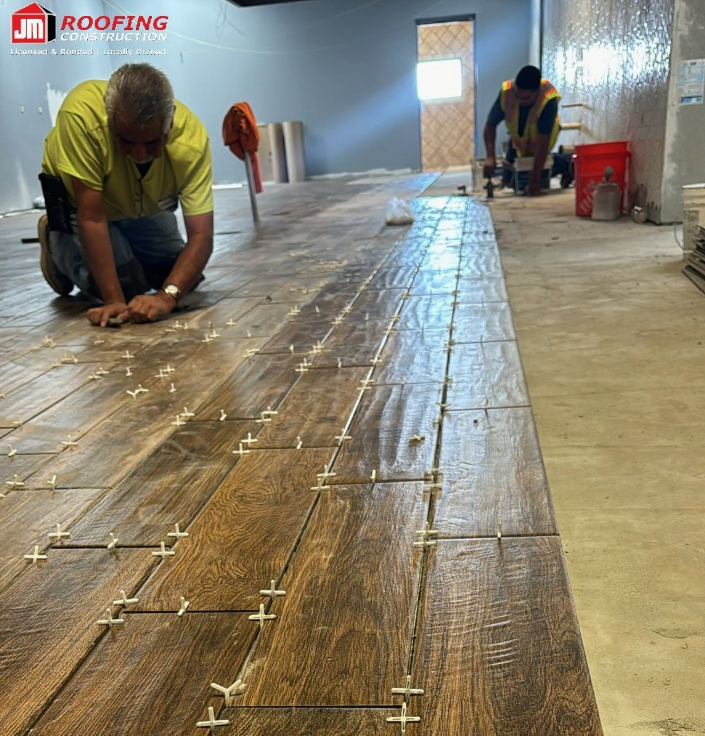 JM Roofing Construction crew installing wood-look plank tile flooring with tile spacers in El Paso, TX